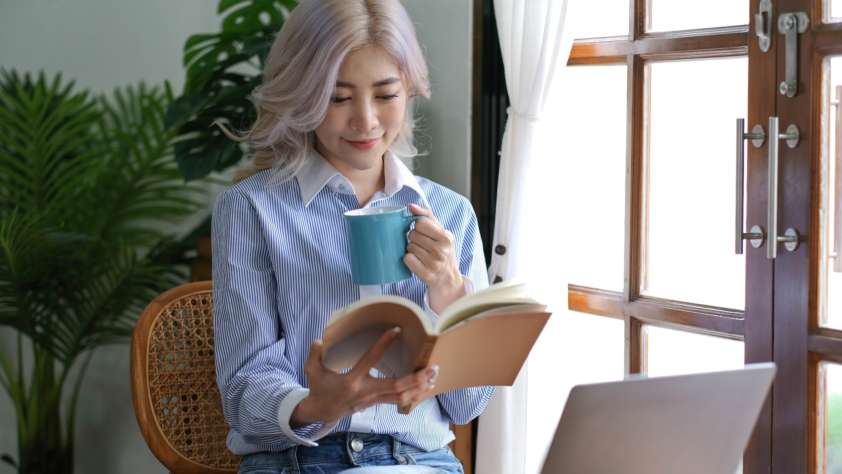 Asian woman reading a book and drinking coffee in the morning.