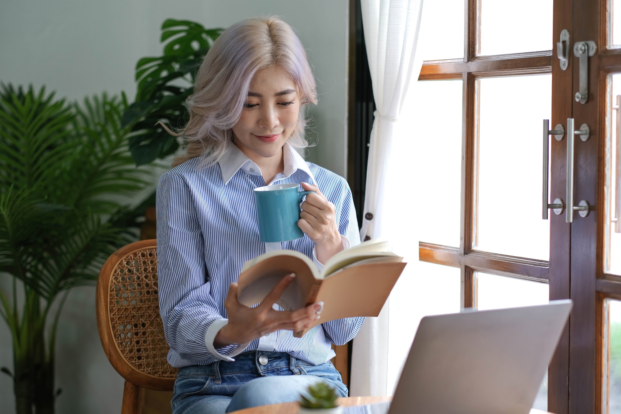 Asian woman reading a book and drinking coffee in the morning.